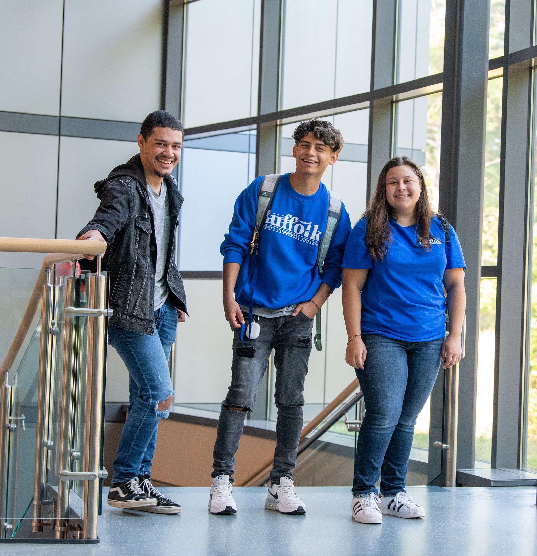 Three Suffolk students standing at the top of a staircase in blue shirts