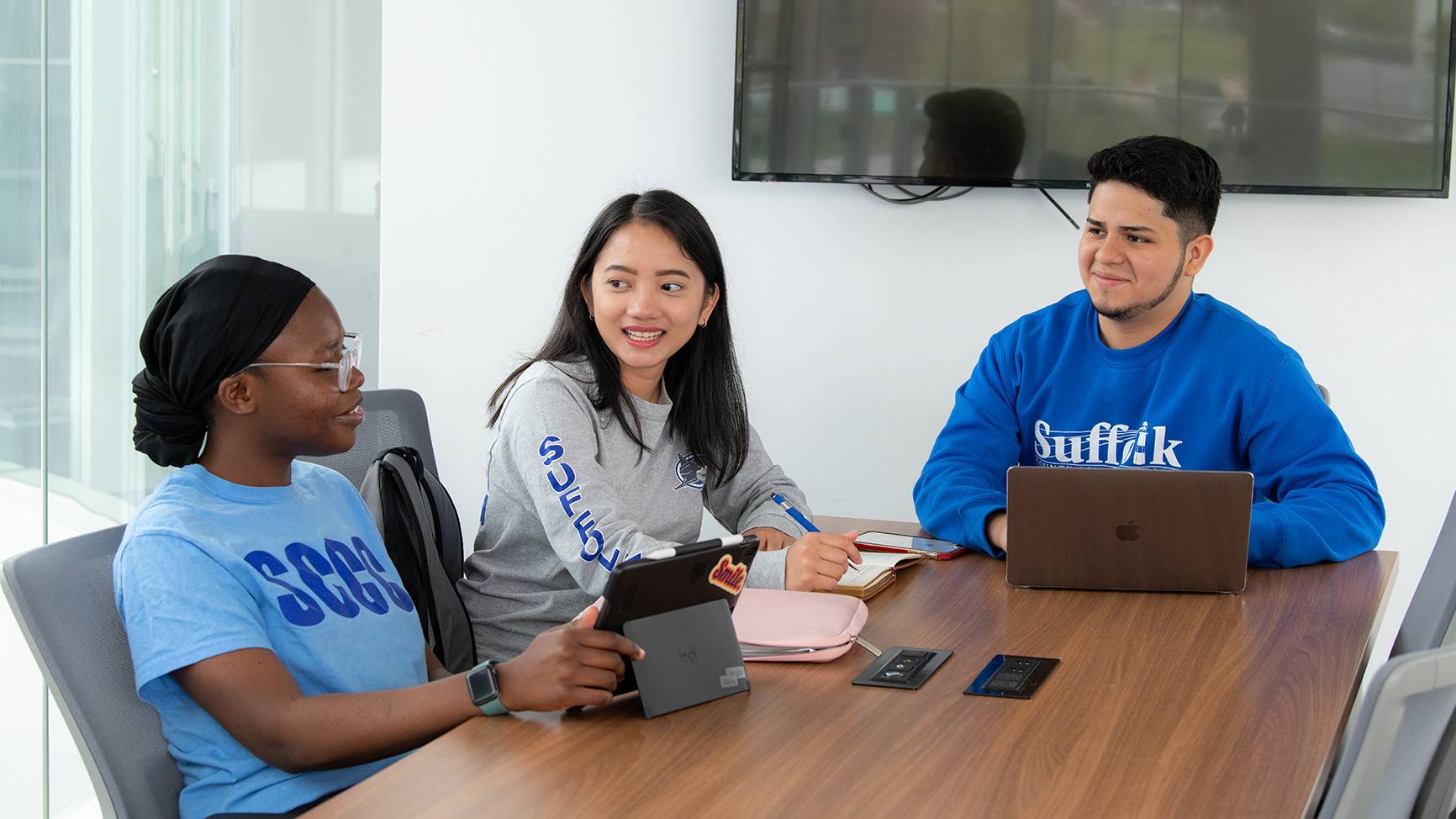 Three students sitting together at a desk with laptops