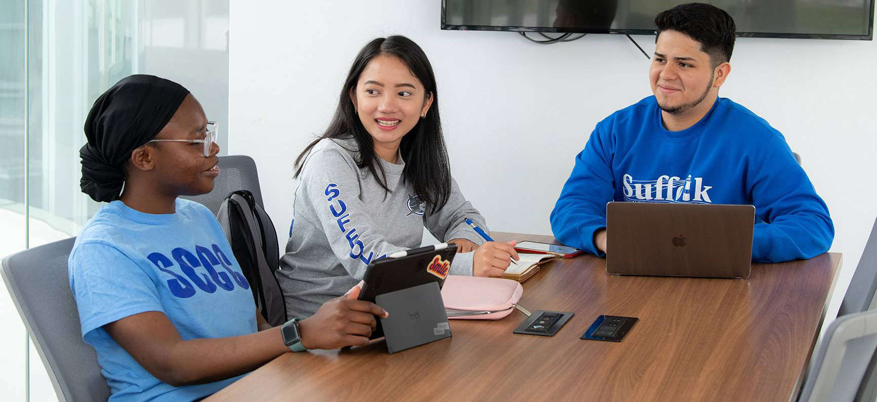 Three students sitting at a table looking at a computer.